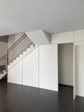 Weiße Treppenverkleidung aus Trennwandelementen mit offener Tür unter einer Treppe
